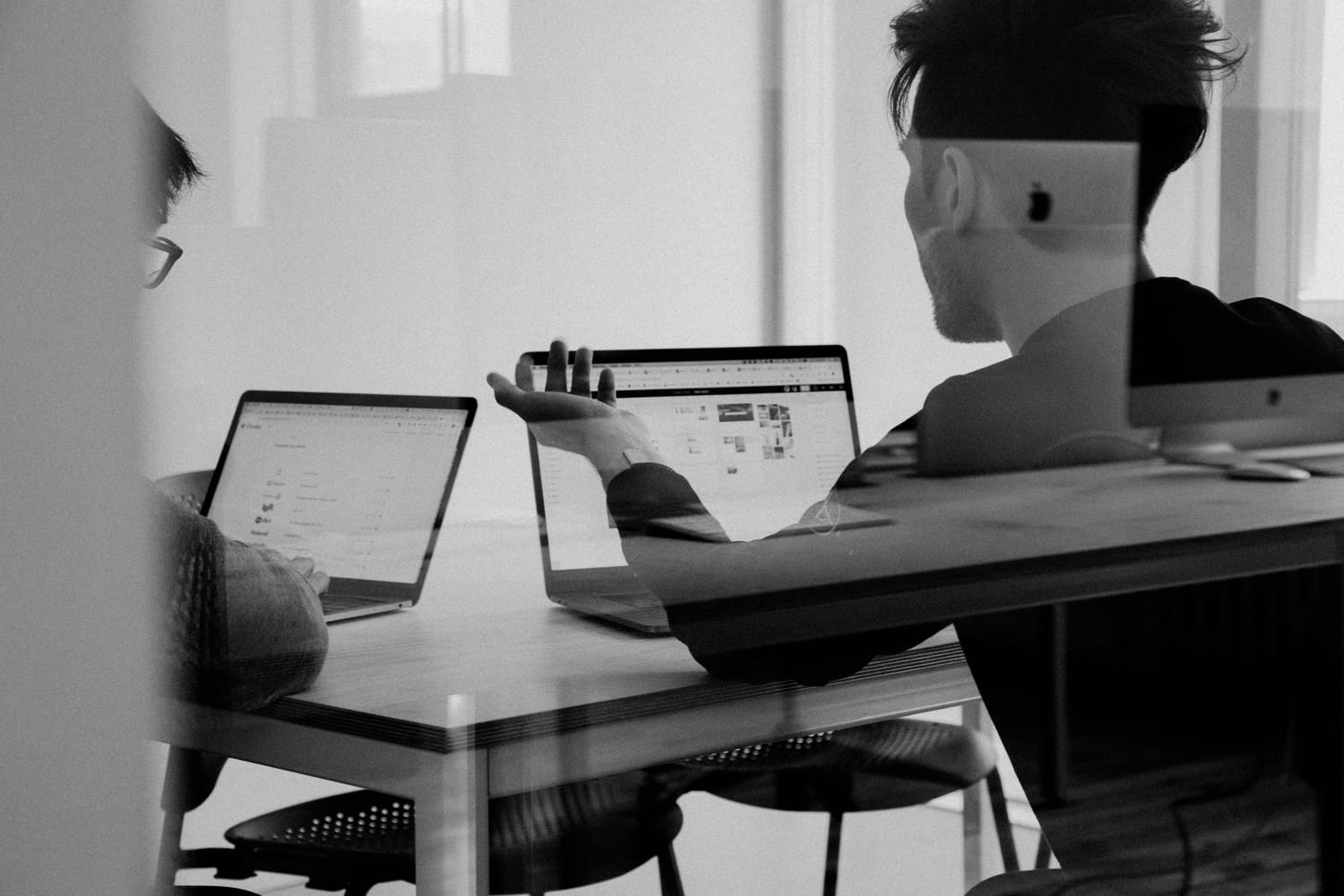 Dos personas del estudio trabajando con portátiles en una mesa, en blanco y negro.